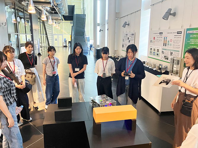 技術体験展示を囲み、実演を交えた説明を受ける参加者の様子